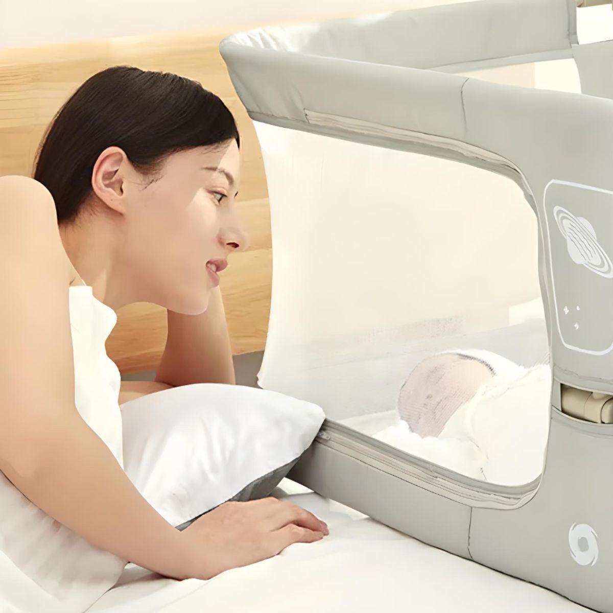 Mother watching baby sleeping safely in NightNest Bedside Rail with breathable mesh barrier