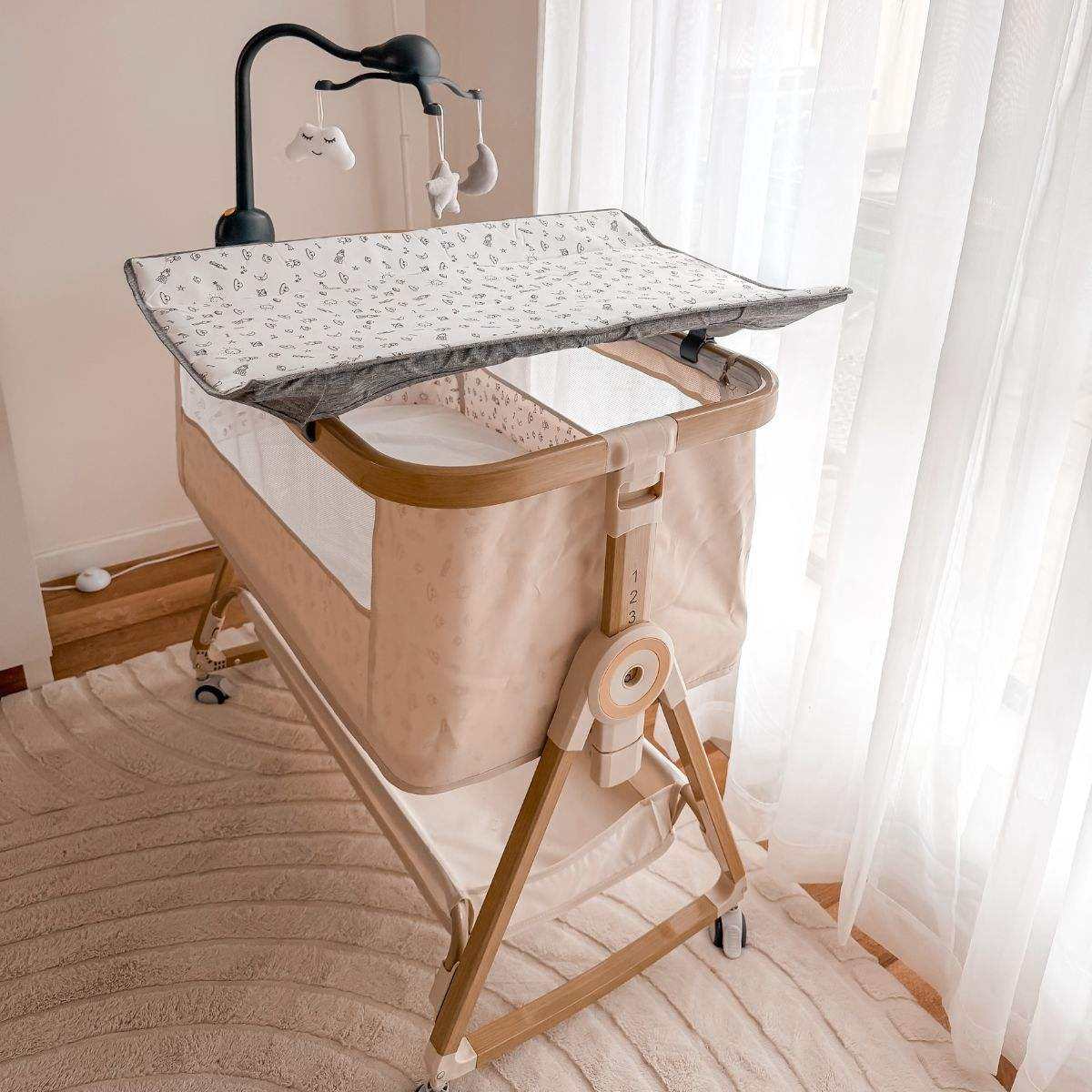 Baby Bassinet & Bedside Co-Sleeper in beige linen-cotton blend with wood-grain steel frame, mesh sides, and detachable canopy with toys